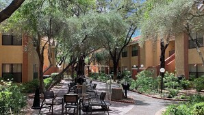 An outdoor patio area with tables and chairs, surrounded by trees and greenery, with buildings in the background. - Two bedroom deluxe resort at West flamingo Bay resort Las Vegas (Las Vegas)