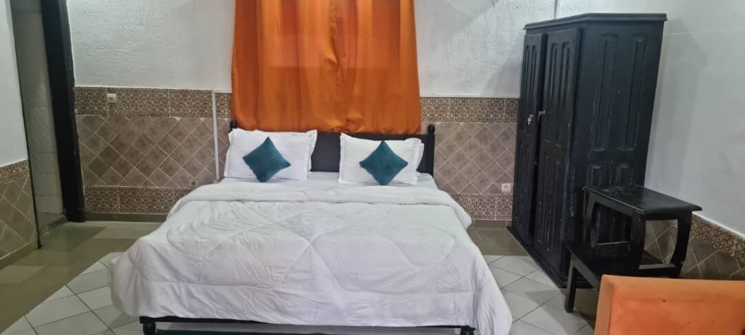 A bed with white bedding and teal pillows, a dark wooden wardrobe, and a small table.
