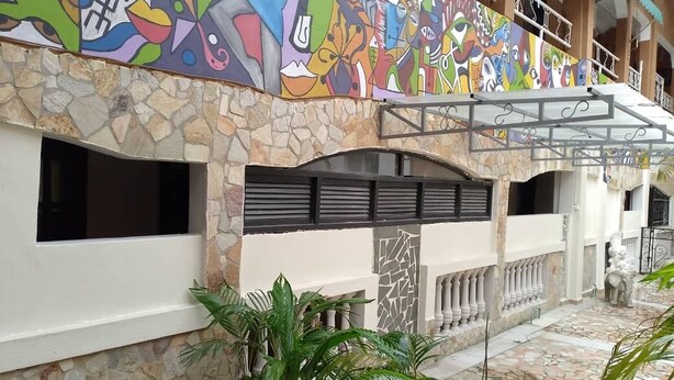 A building with a stone facade, a colorful mural, and a covered outdoor area with plants.