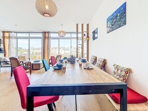 Ein zeitgemäßer Essbereich mit Holztisch, roten und blauen Stühlen und Blick auf Gebäude durch große Fenster.