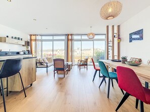 Ett modernt kök med en stor köksö, en matplats med färgglada stolar och stora fönster med utsikt över staden.