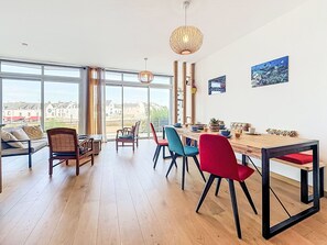 Ein geräumiger Essbereich mit einem Holztisch, bunten Stühlen und großen Fenstern, die Blick auf Gebäude und Grünflächen bieten.