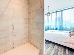 Ein Schlafzimmer mit einem Bett, einer Bank und Blick ins Freie durch transparente Vorhänge.