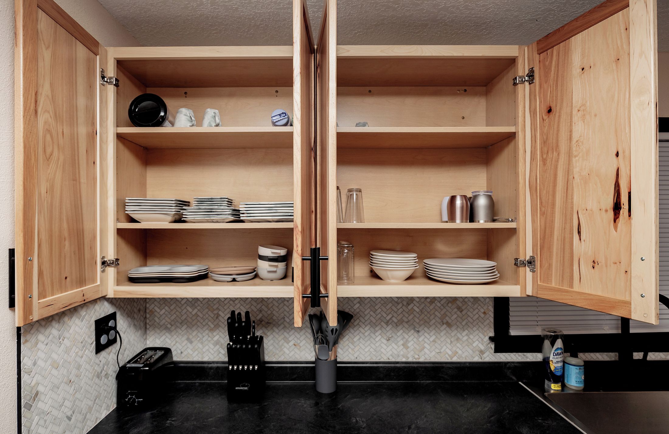 A kitchen with wooden cabinets, black countertops, and various kitchen utensils.