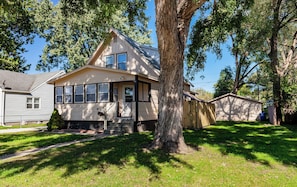 A two-story house with a front porch, a garage, and a large tree in front.