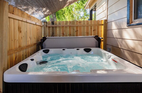 Un jacuzzi con un muelle de madera que lo rodea, un techo de paja y una ventana a la derecha.