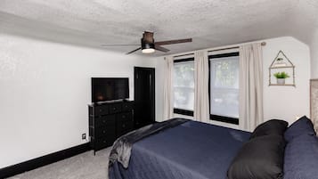 Ein Schlafzimmer mit einem Bett, einem Schminktisch, einem Fernseher und einem Deckenventilator.
