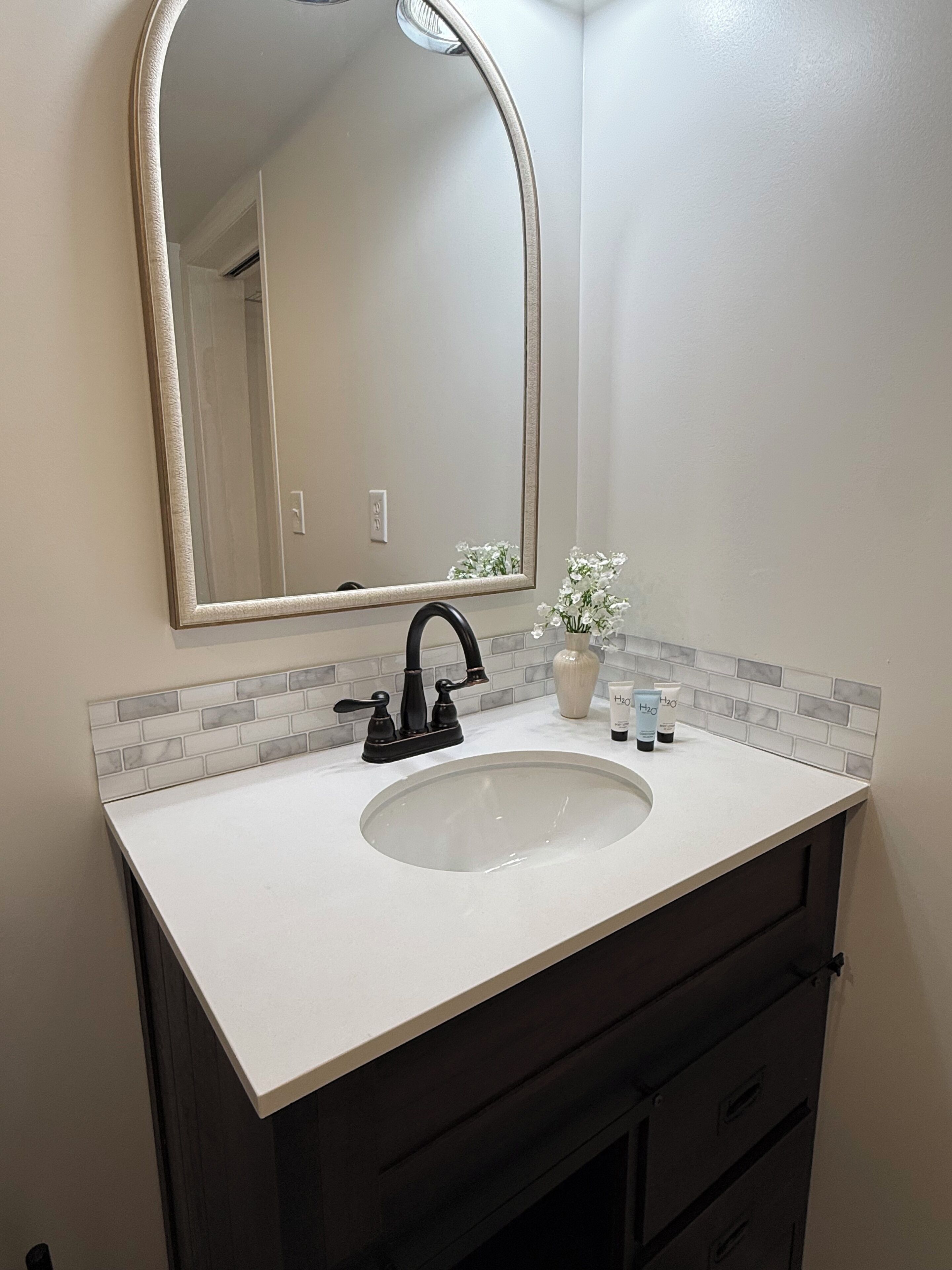 A bathroom with a white sink, black faucet, and a mirror with a beige frame.