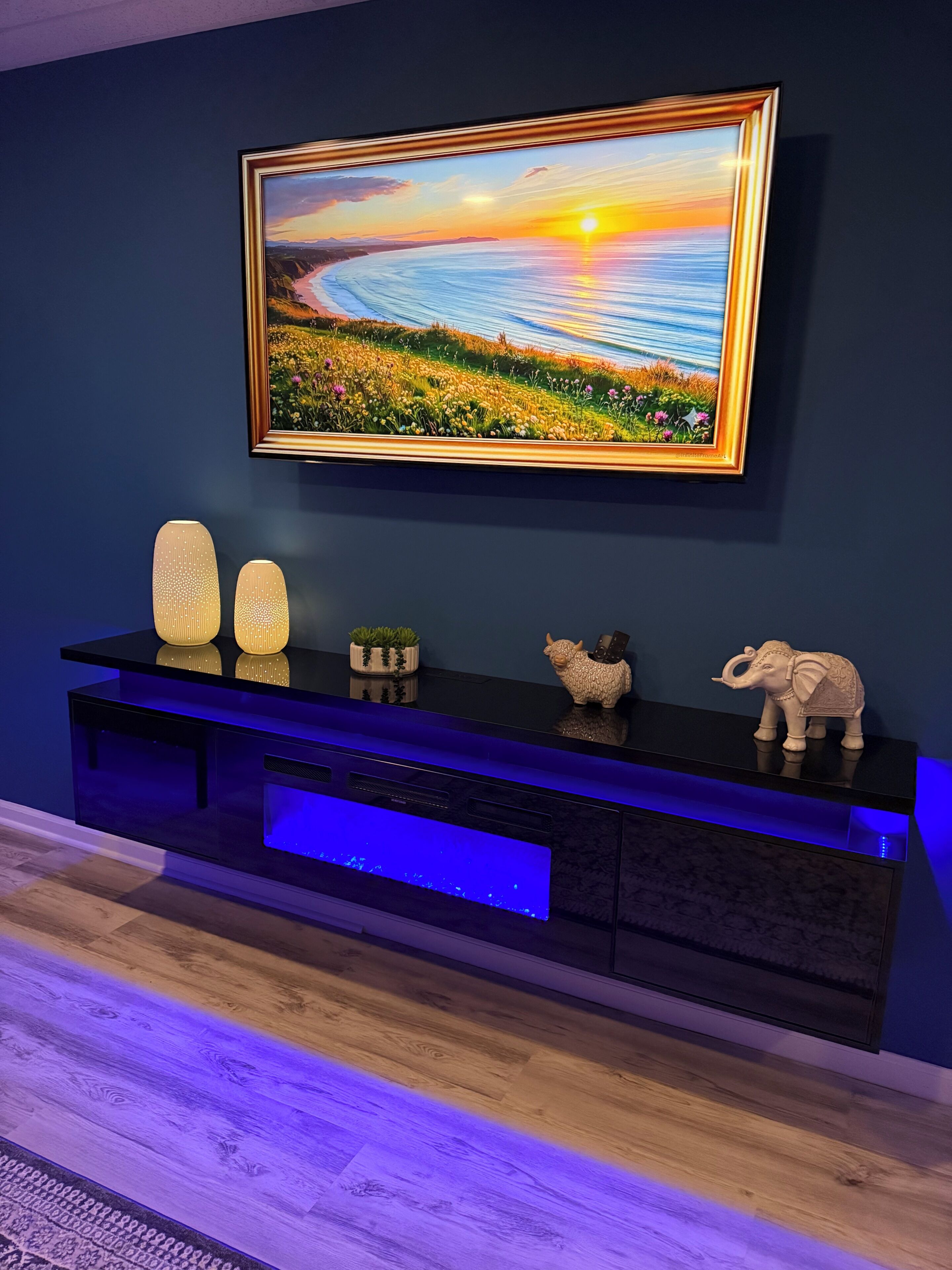 A modern living room with a flat-screen TV mounted on a dark wall, a black entertainment unit with blue lighting, and decorative items including a small elephant figurine.