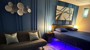 Une chambre à coucher moderne avec un canapé, un lit, une table de chevet, une lampe et un tapis à motifs.