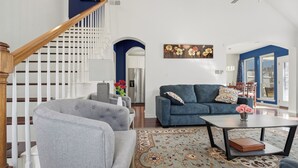 Un salon avec un escalier, un canapé bleu, une table basse et un tapis à motifs.