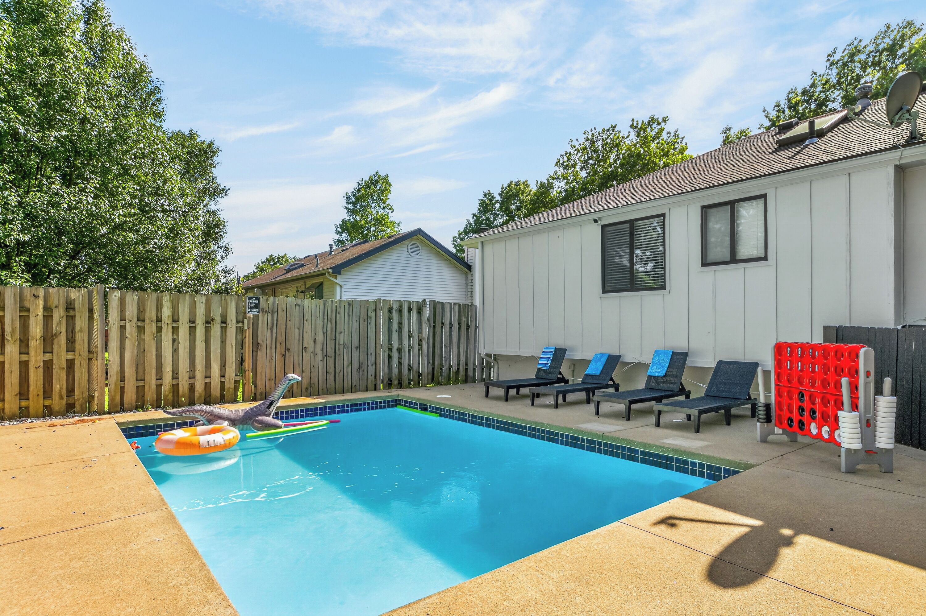 A backyard with a swimming pool, a wooden fence, and a house.