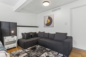 A modern living room with a sectional sofa, a white side table, a patterned rug, and a wall art piece. - The Grand Estate . Private Pool . Sleeps 10 . Events Welcome (Grandview)