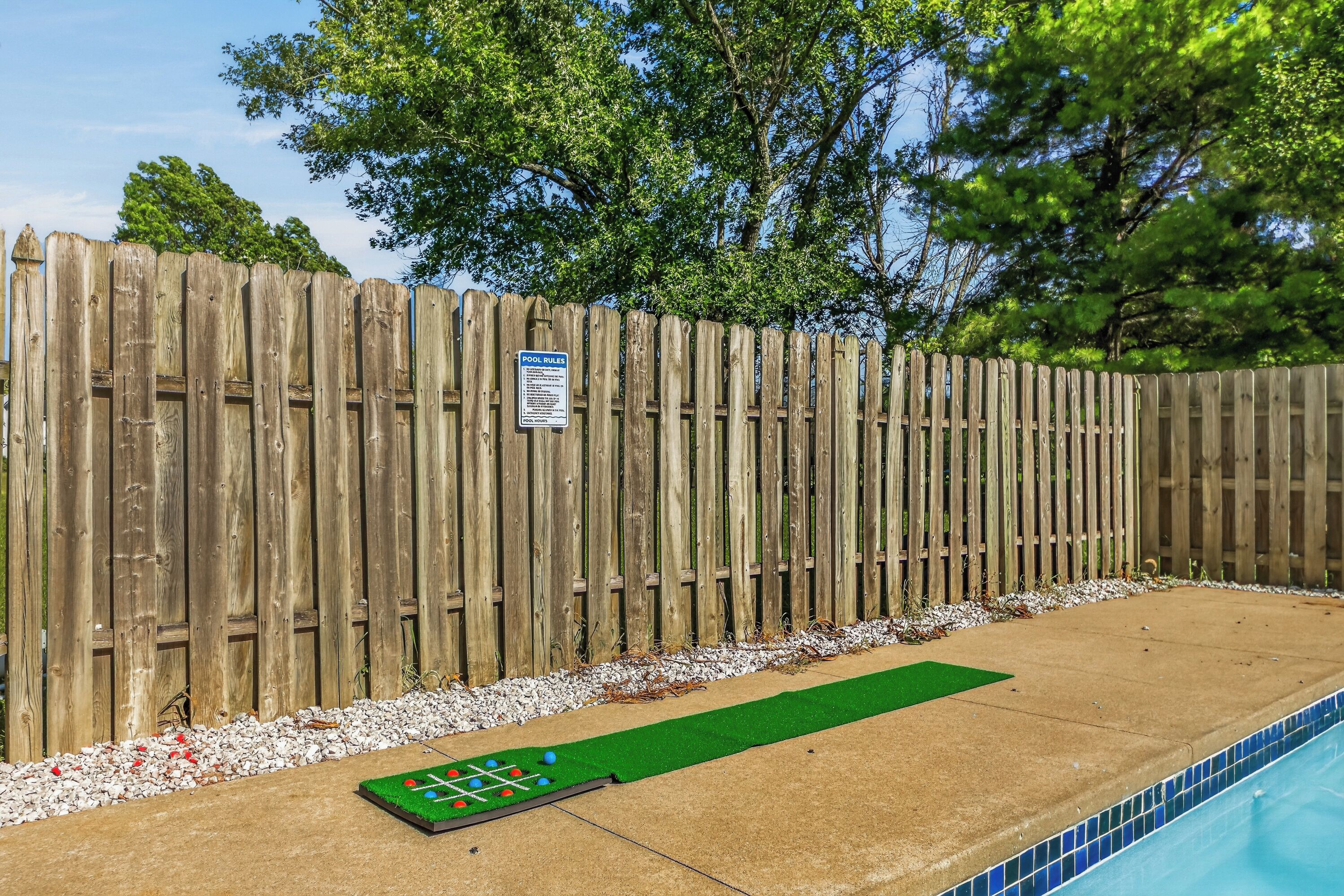 A wooden fence with a pool area, including a green mat and a pool table.