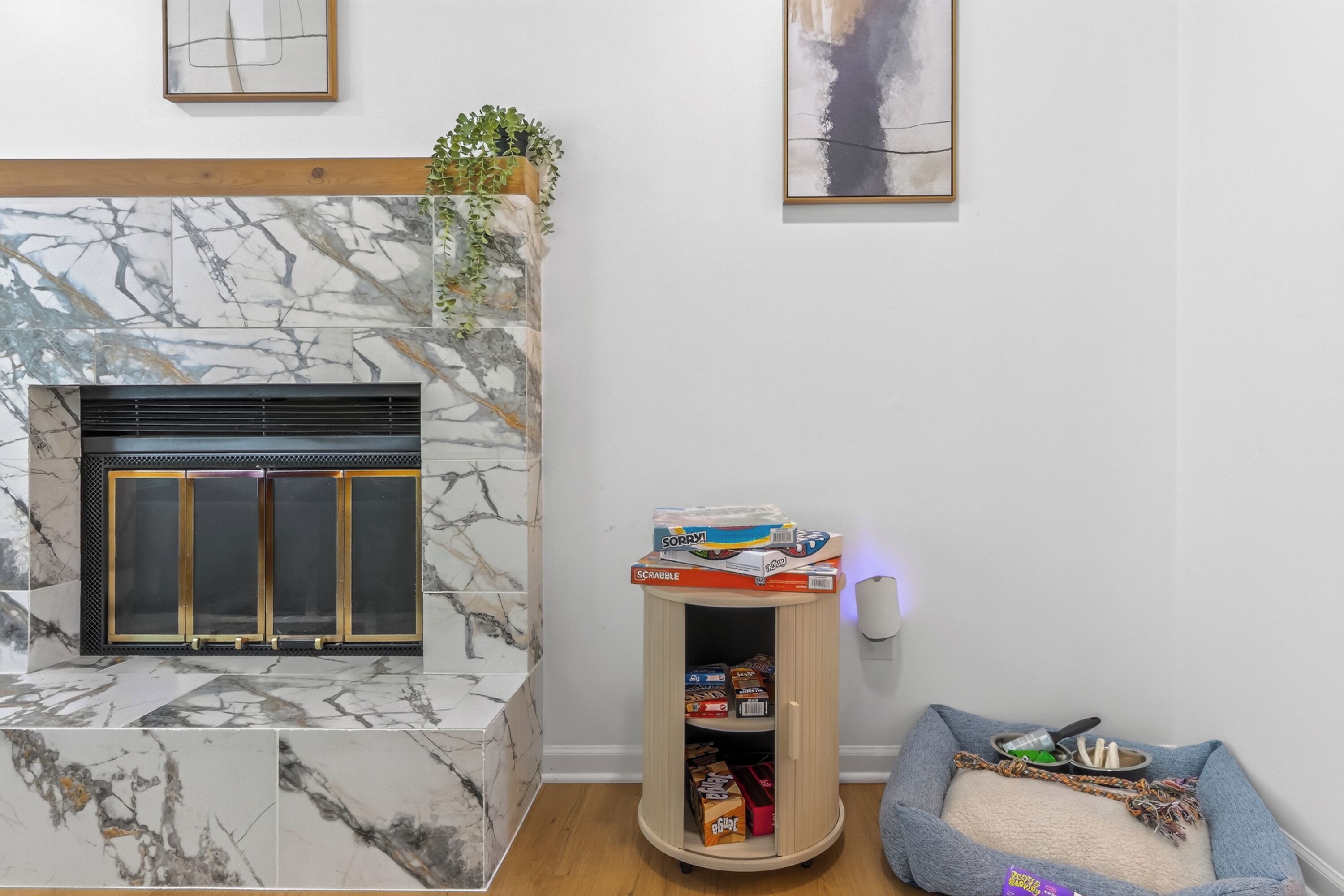 A living room with a marble fireplace, a wooden cabinet with snacks, and a pet bed.