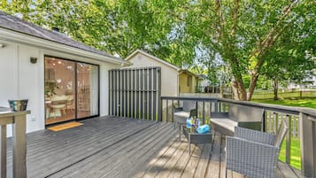 Terraza de madera con mobiliario exterior, puerta corrediza de vidrio y área cercada.