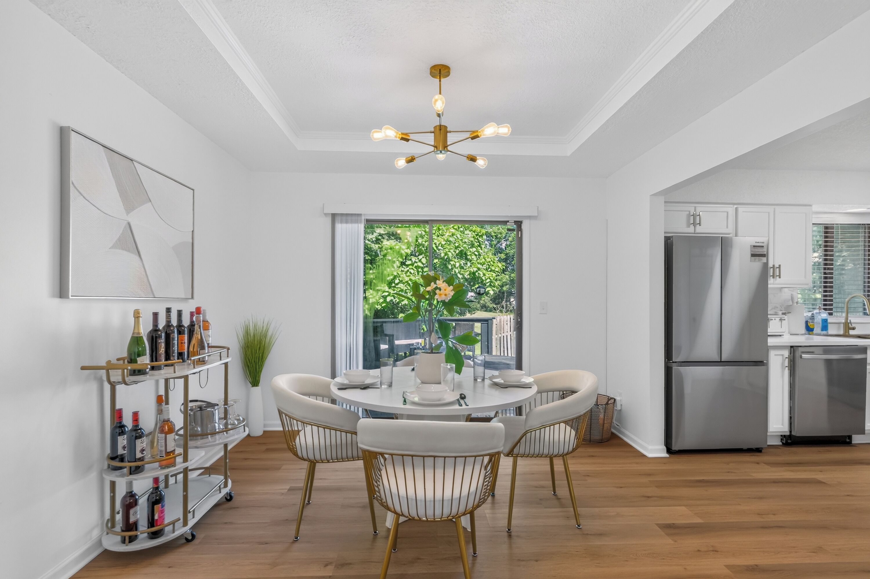 Een moderne keuken met roestvrijstalen apparatuur, een eethoek met een ronde tafel en stoelen, en een groot raam met uitzicht op groen.