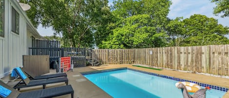 A backyard with a swimming pool, lounge chairs, and a wooden fence.