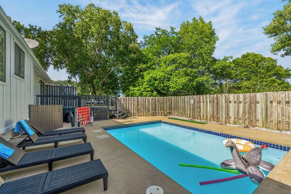 A backyard with a swimming pool, lounge chairs, and a wooden fence.