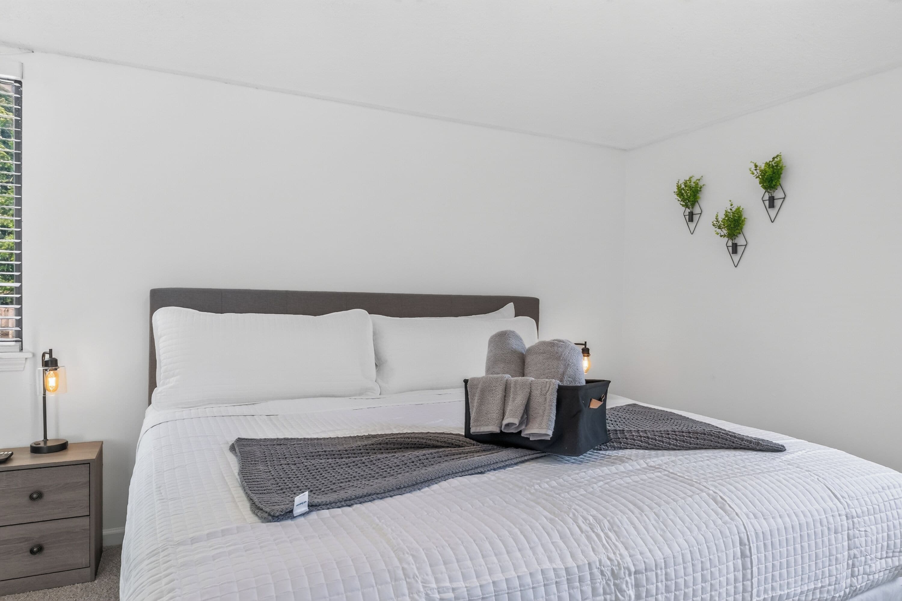 A neatly made bed with pillows, a blanket, and towels, a bedside table with a lamp, and wall-mounted planters.