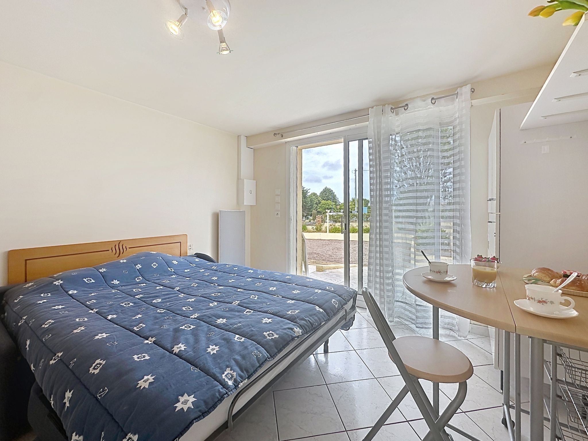 Une chambre avec un lit, une table où sont disposés des éléments pour le petit-déjeuner, et une vue à travers une porte vitrée.