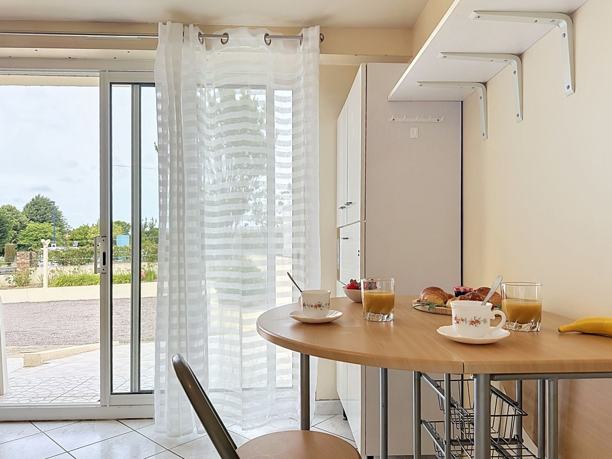 Un coin repas avec une table mise pour le petit-déjeuner, comprenant un bol de fruits, un verre de jus d’orange, un croissant et une tasse de café.