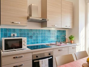 A kitchen with a microwave, oven, and sink, with blue tiles and wooden cabinets. - Apartment DaDo by Interhome (Alghero)