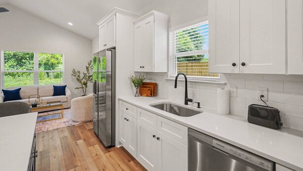 Una cocina moderna con gabinetes blancos, un refrigerador de acero inoxidable, un lavavajillas y una ventana con persianas.