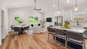 Una cocina moderna con una isla central, piso de madera y muebles blancos.