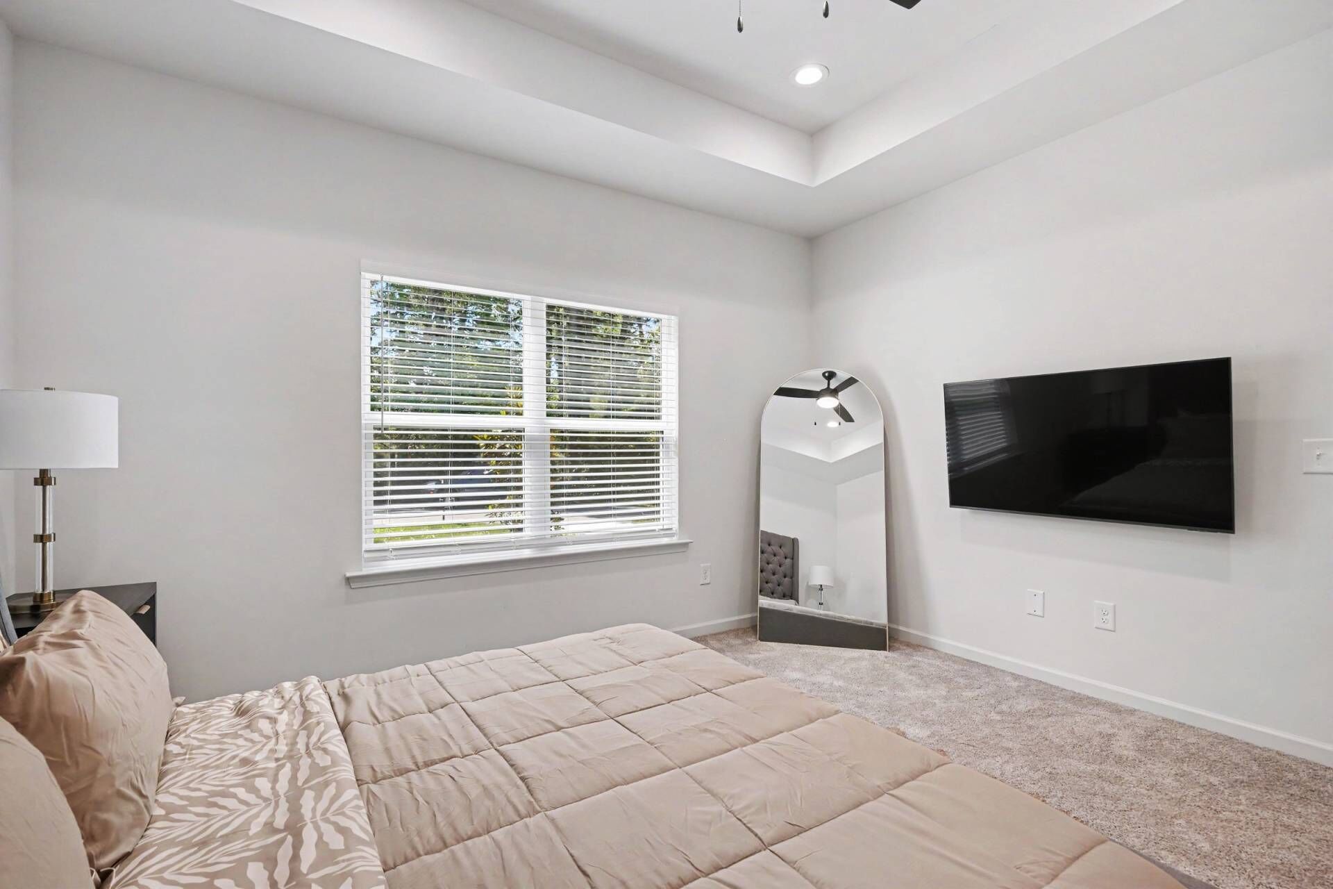 Un dormitorio con una cama, ventilador de techo, televisión y ventana con persianas.