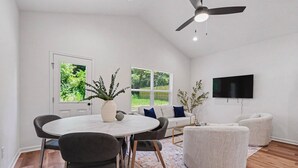 Una sala de estar moderna con una mesa redonda de comedor, dos sofás, un televisor y un ventilador de techo.