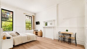 Quarto com cama, mesa de cabeceira, luminária e escrivaninha com cadeiras.