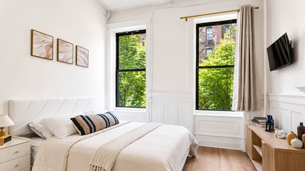 Quarto com cama, mesas de cabeceira, televisão e janelas com cortinas.