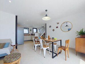 Eine moderne Küche mit weißen Schränken, einem Esstisch mit Stühlen, einer Treppe und einem Wohnbereich mit einer Couch und einem gemusterten Hocker.
