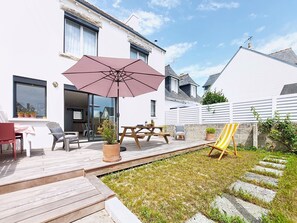Eine Terrasse mit Tisch, Stühlen, einem großen Sonnenschirm und einem gelb-gestreiften Sessel.