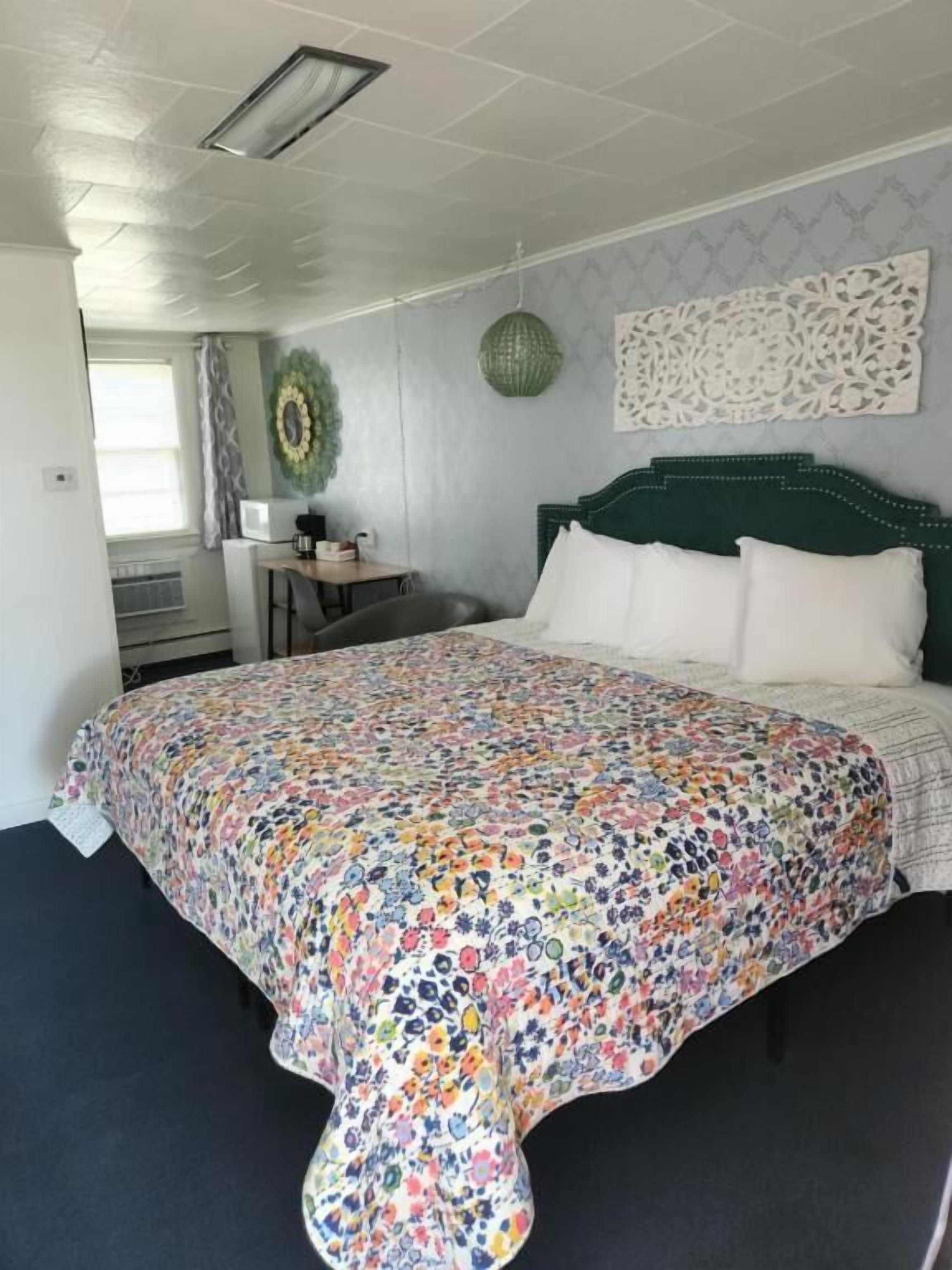 A bedroom with a floral bedspread, a green headboard, and a decorative wall piece.