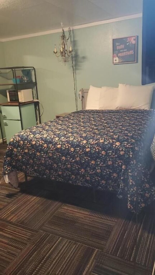A bed with floral bedding, a chandelier, a wall-mounted sign, and a wooden floor.