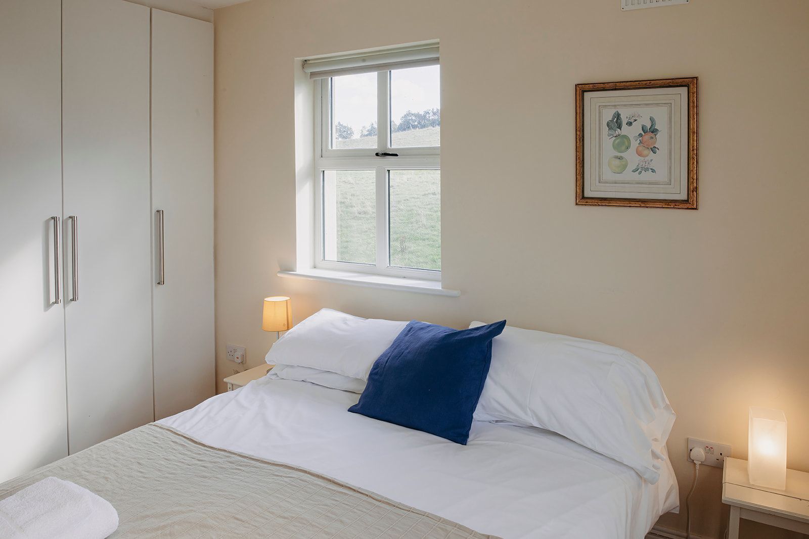 A bedroom with a bed, a window, a bedside lamp, a nightstand, and a wardrobe.