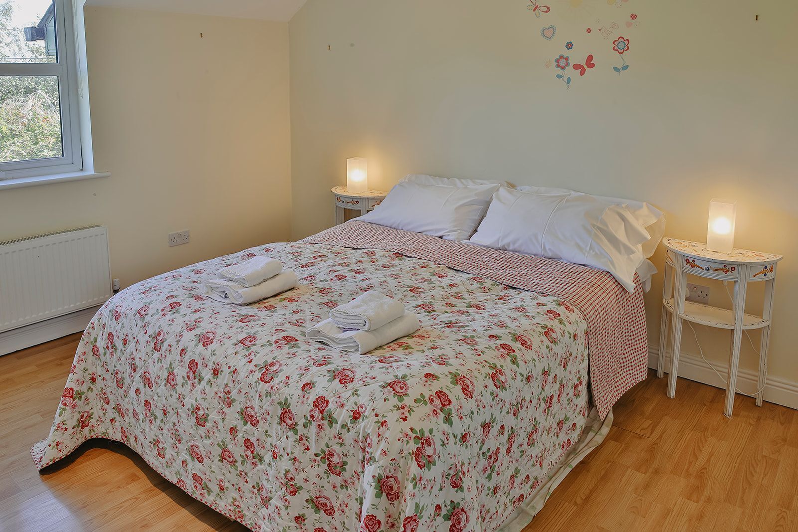 A neatly made bed with floral bedding, two bedside lamps, and a window with a view.