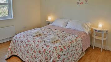 A neatly made bed with floral bedding, two bedside lamps, and a window with a view.
