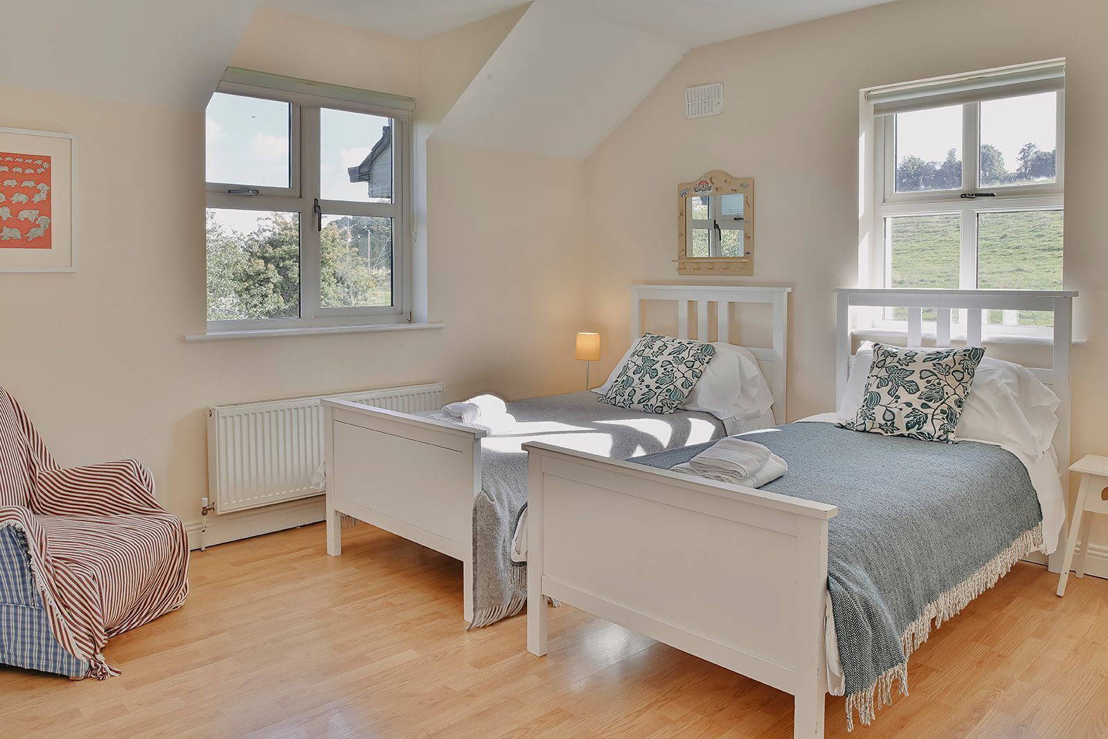 Une chambre avec deux lits simples, un radiateur, une chaise et deux fenêtres.
