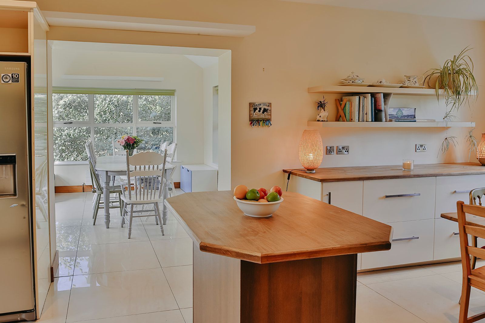 A modern kitchen with a wooden island, a dining area with chairs, and a view through a glass door.