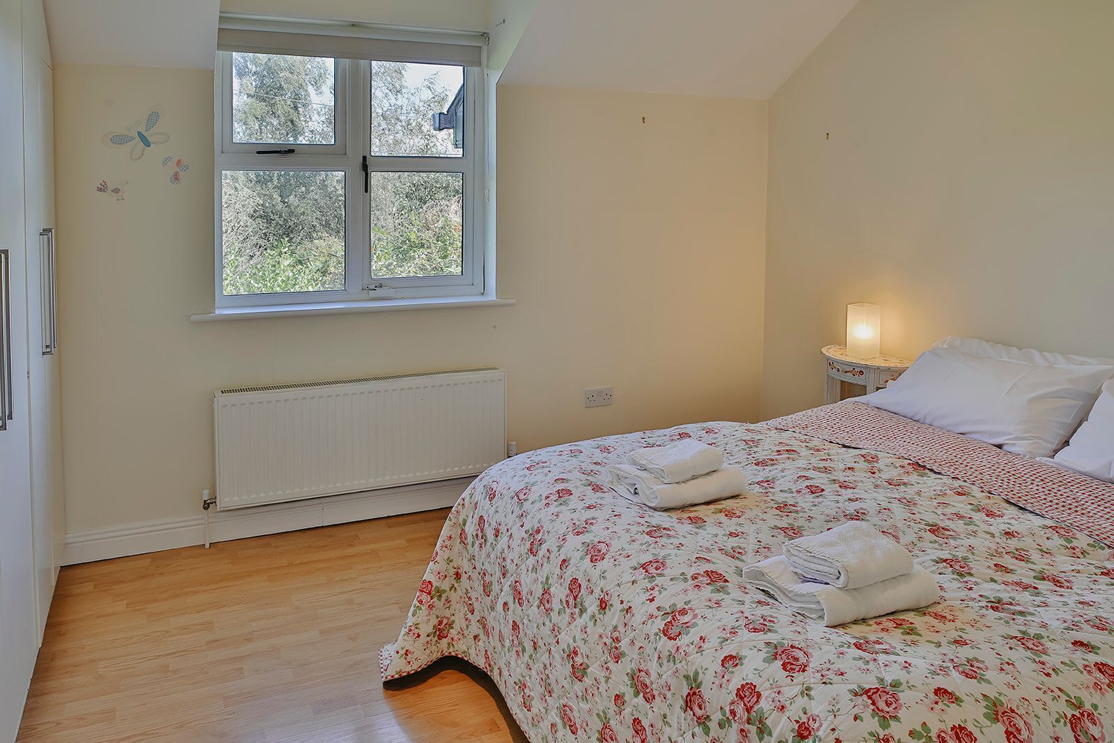 A bedroom with a bed, a window, a radiator, and a bedside table with a lamp.