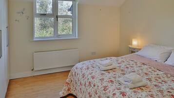 A bedroom with a bed, a window, a radiator, and a bedside table with a lamp.