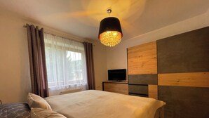 Une chambre à coucher avec un lit, un téléviseur posé sur une commode en bois et une fenêtre avec des rideaux.