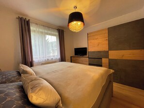 Une chambre à coucher avec un lit, un téléviseur posé sur une commode en bois et une fenêtre avec des rideaux.