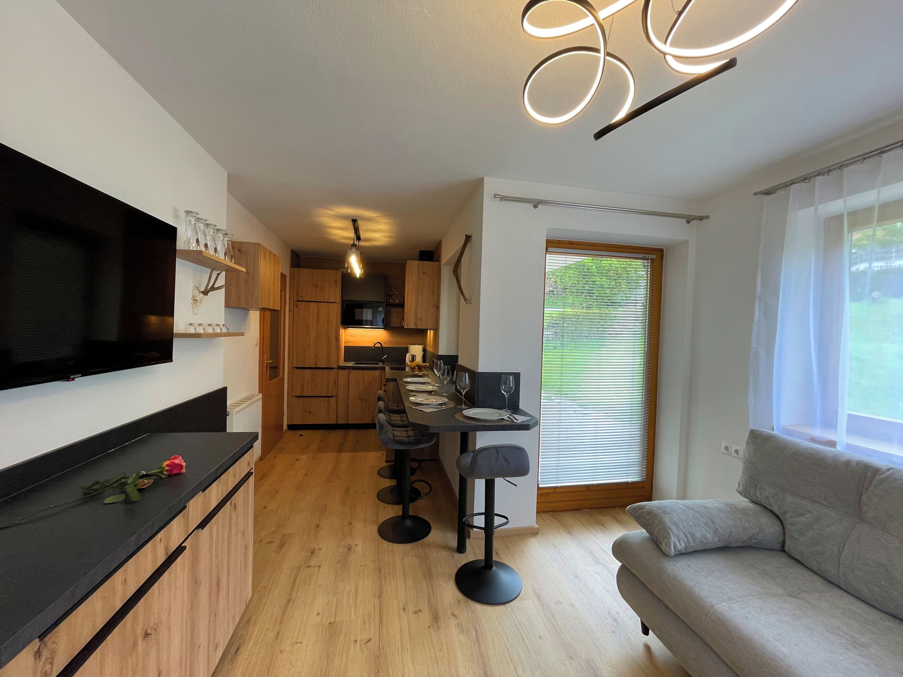 A modern kitchen with wooden cabinets, a black countertop, and a dining area with a bar stool and table set.