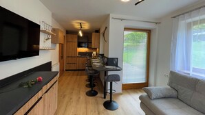 Une cuisine moderne avec des meubles en bois, un plan de travail noir et un coin repas comprenant un tabouret de bar et une table.