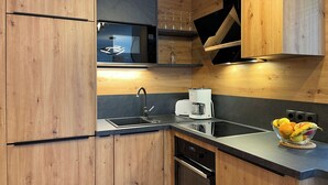 Une cuisine moderne avec des meubles en bois, un four à micro-ondes, une machine à café et un panier à fruits.