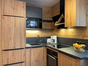 Une cuisine moderne avec des meubles en bois, un four à micro-ondes, une machine à café et un panier à fruits.